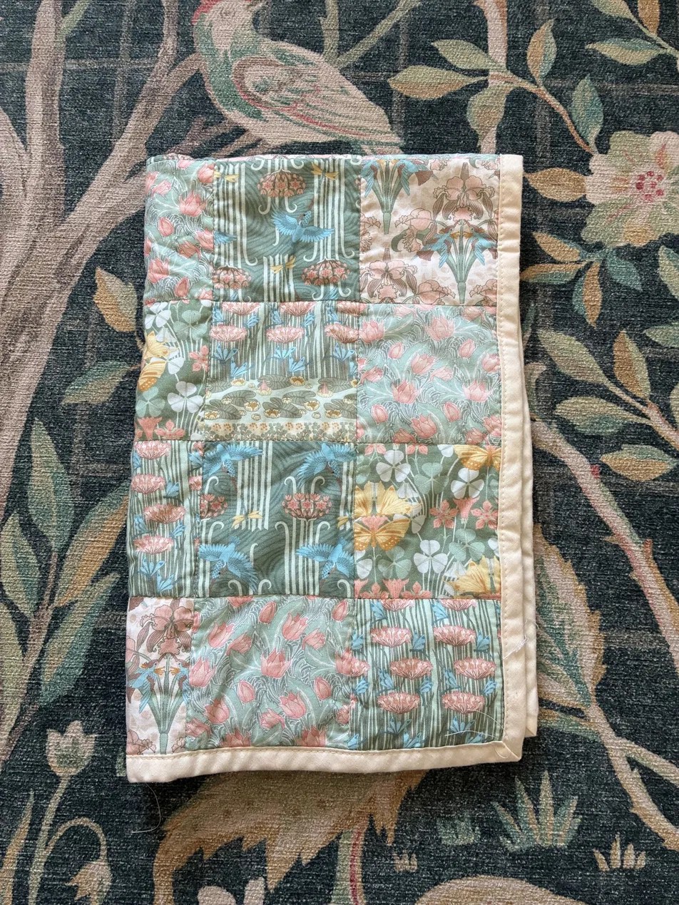 A folded quilt made from art nouveau floral and botanical fabrics in green, pink and gold